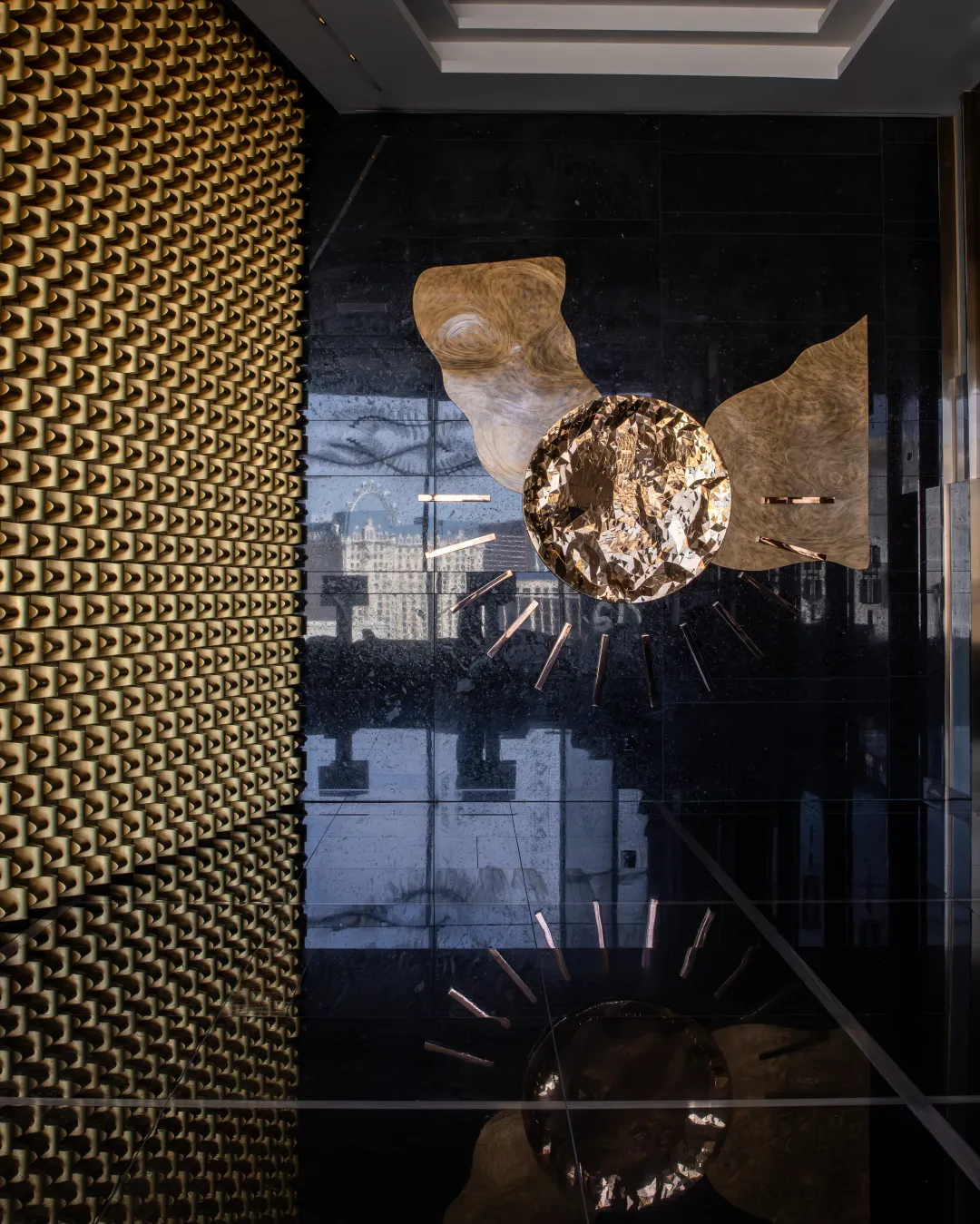 Sculptural gold artwork reflected against a dark stone wall
